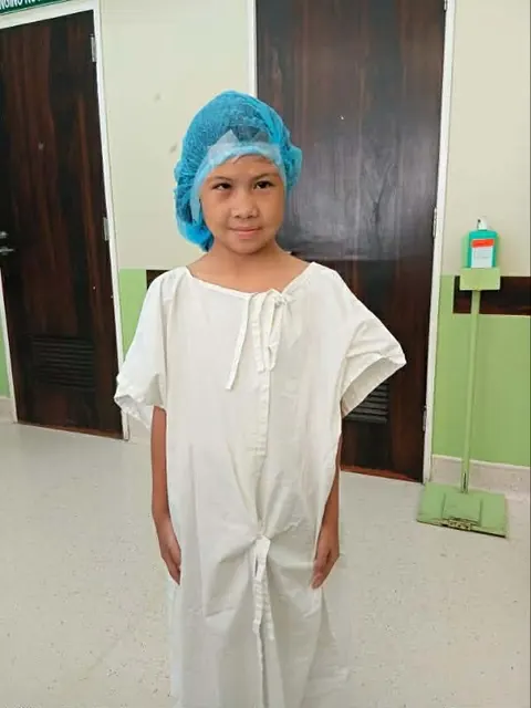 Angela in a hospital gown and cap on the day of her surgery