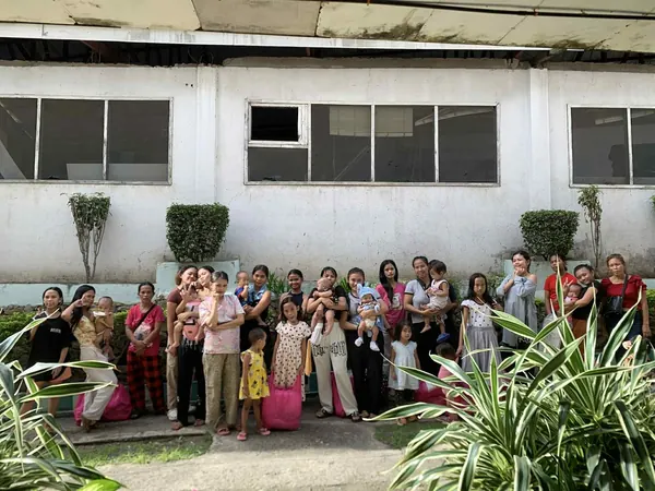 A large group of girls and young mothers, many holding babies, outside a community building in Cebu